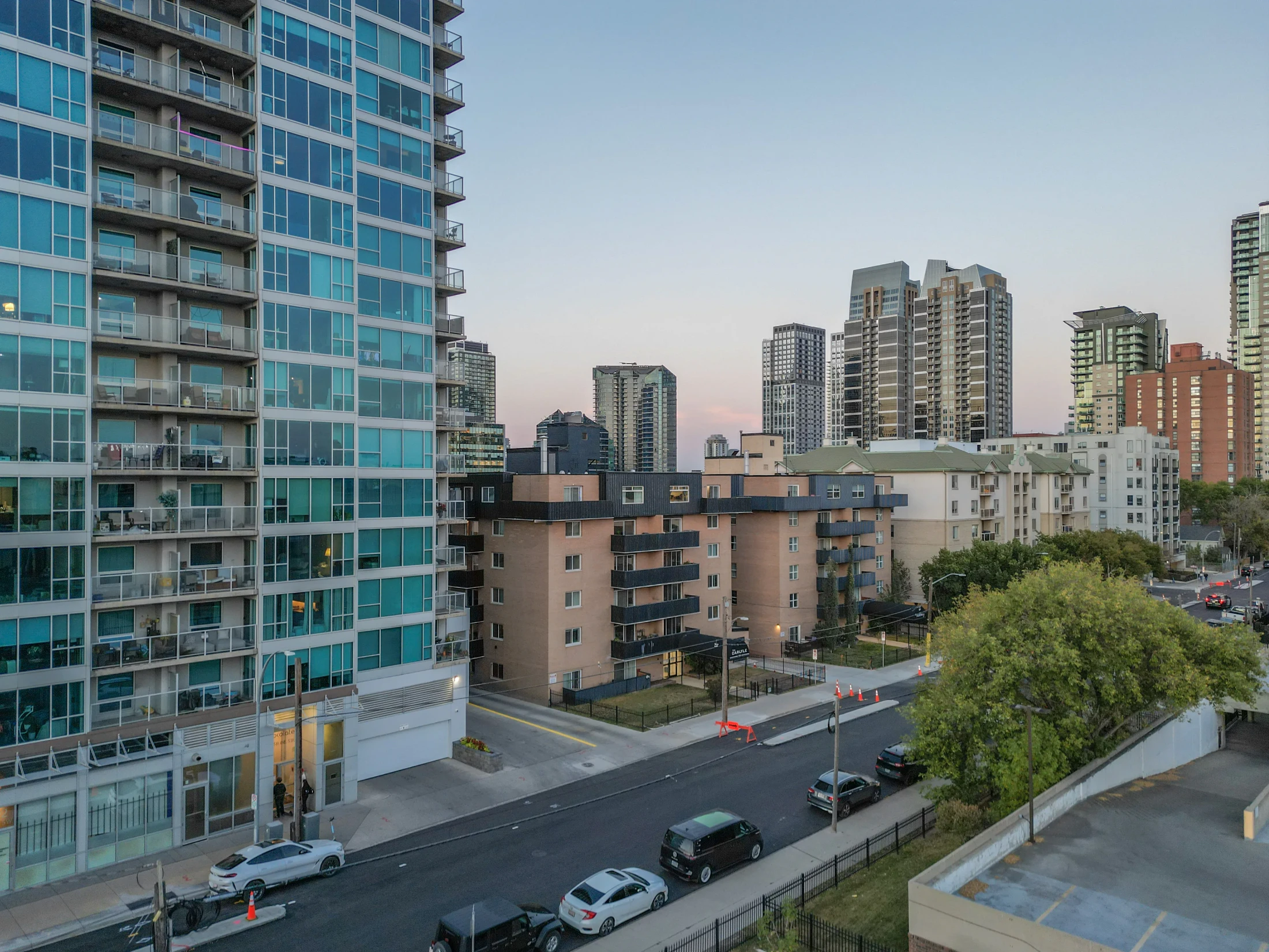 Glass condo tower beside older apartment buildings and trees