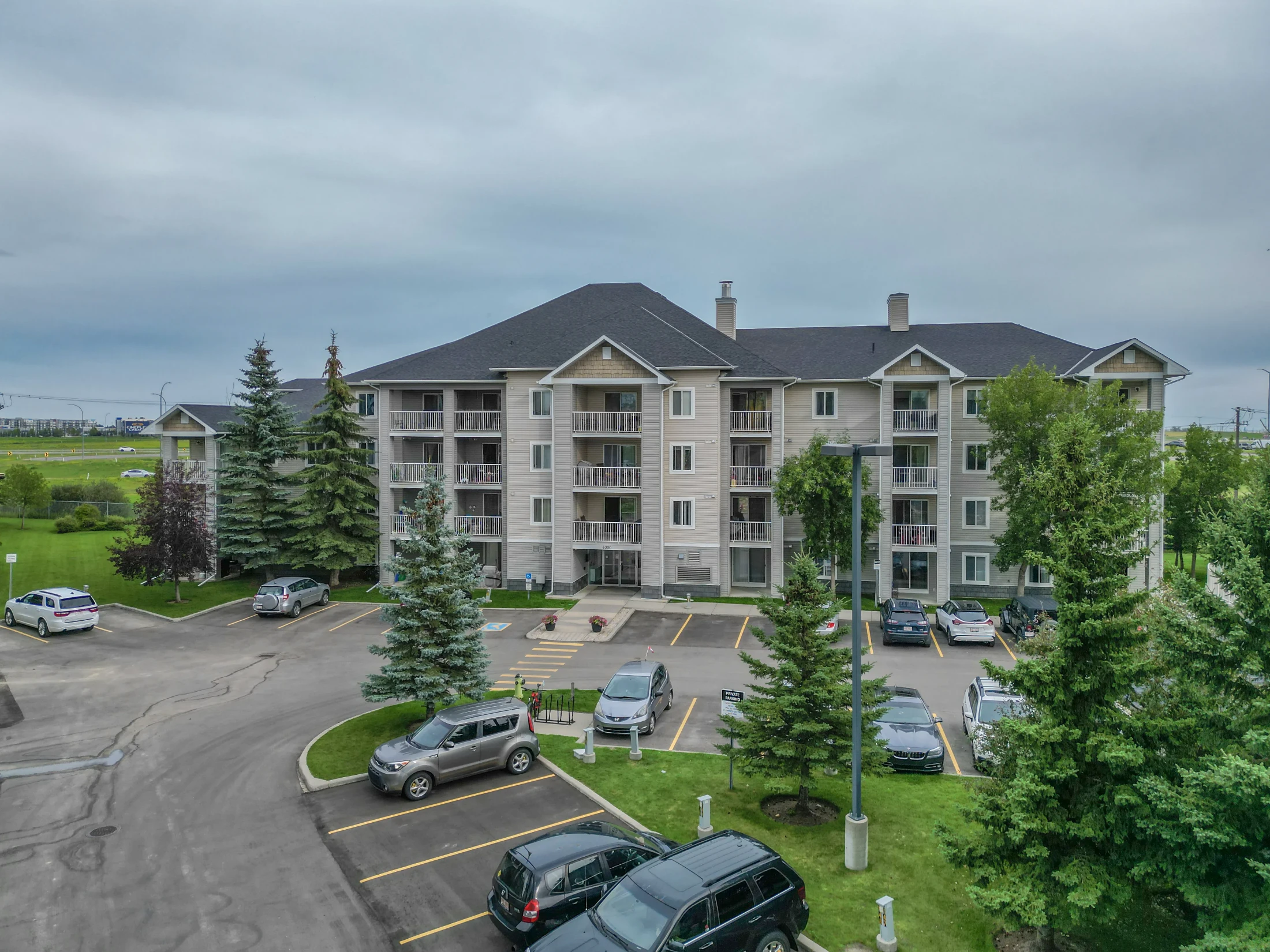 Three-storey condo building with balconies and tall spruce trees