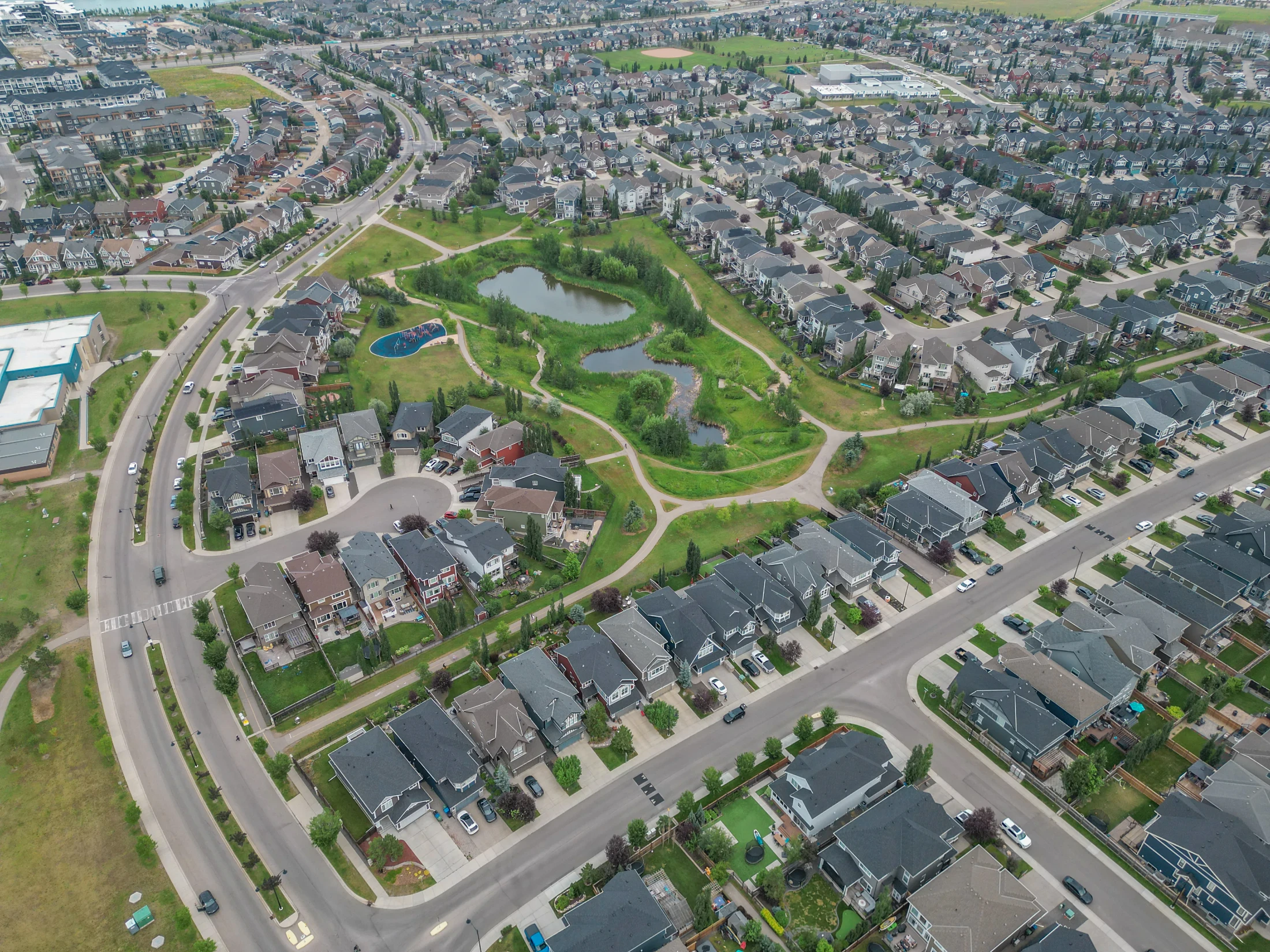 Aerial view of homes around a green park with a pond in northwest Calgary