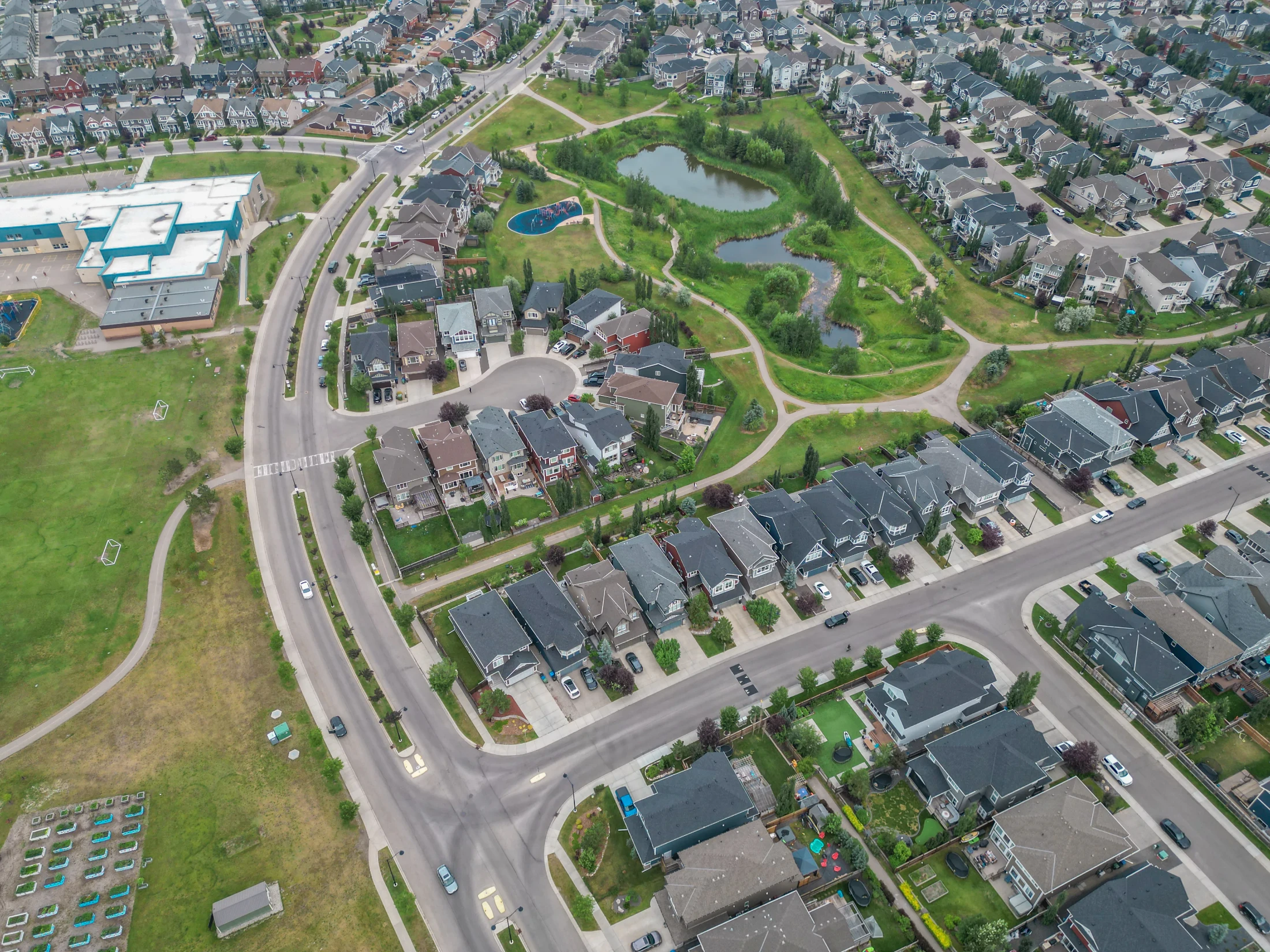 Aerial view of a green space with a pond beside new detached homes in northwest Calgary