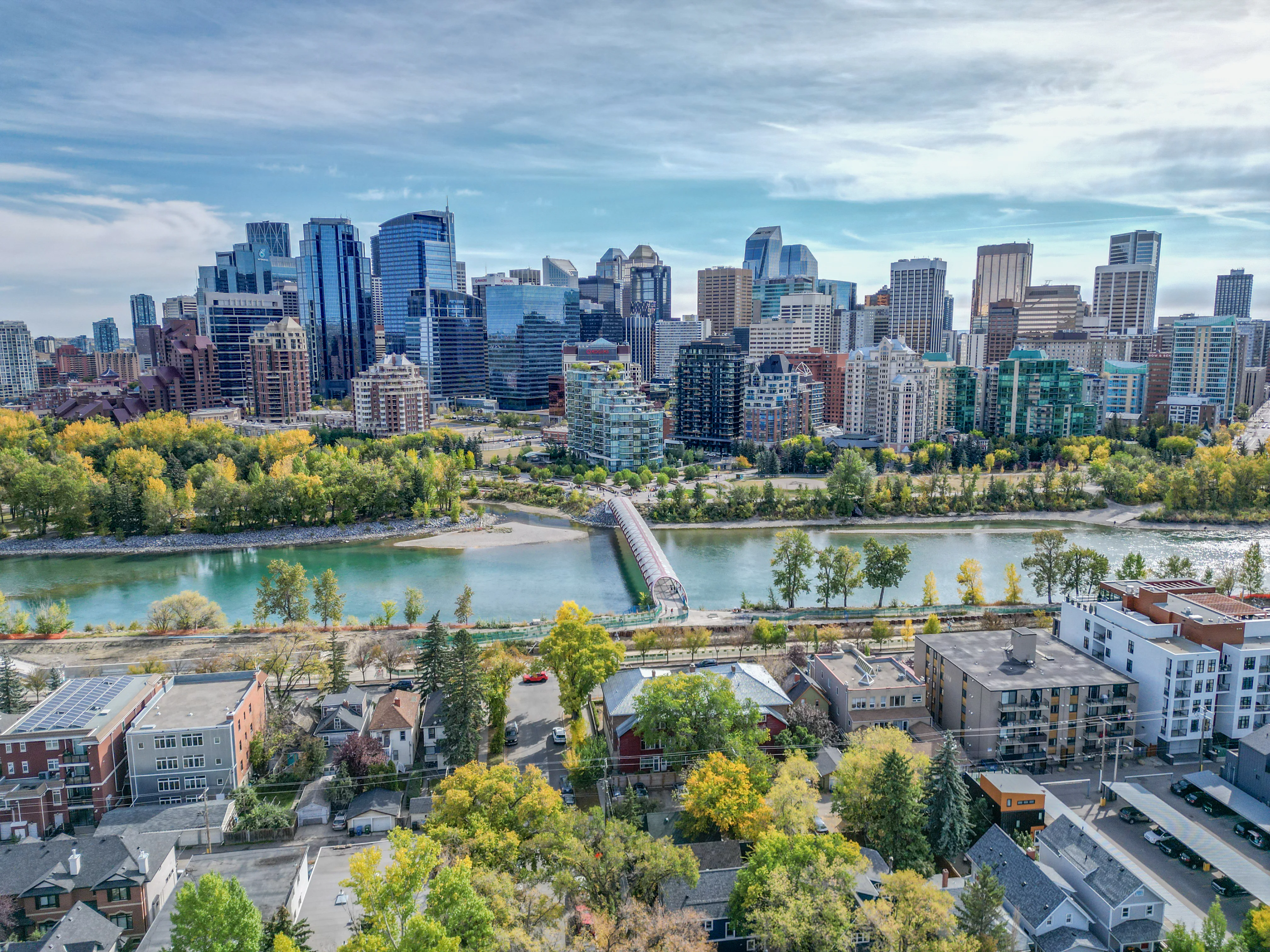 Footbridge over the Bow River with riverside homes and downtown towers