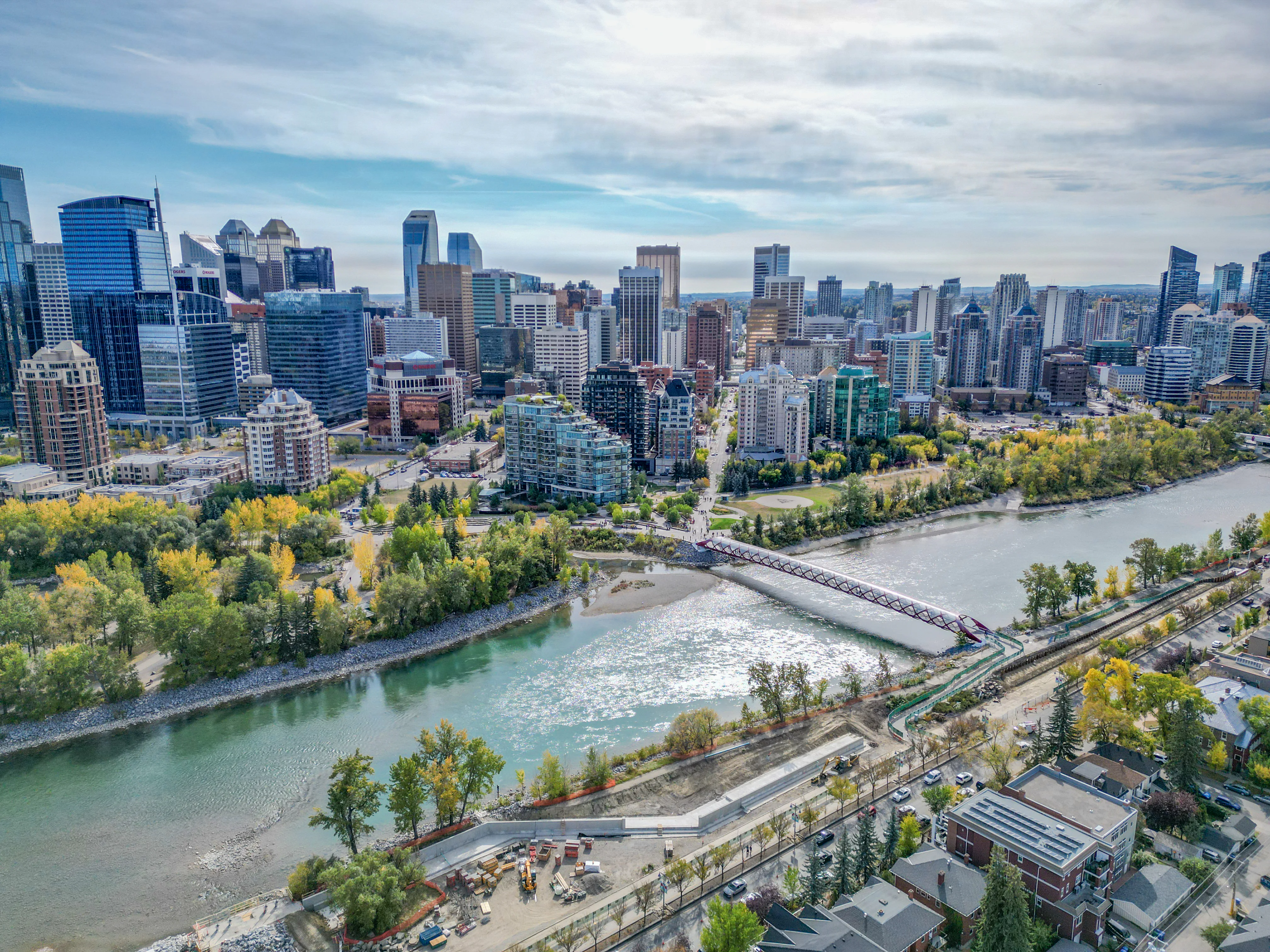 Riverside pathway along the Bow River with trees and city towers