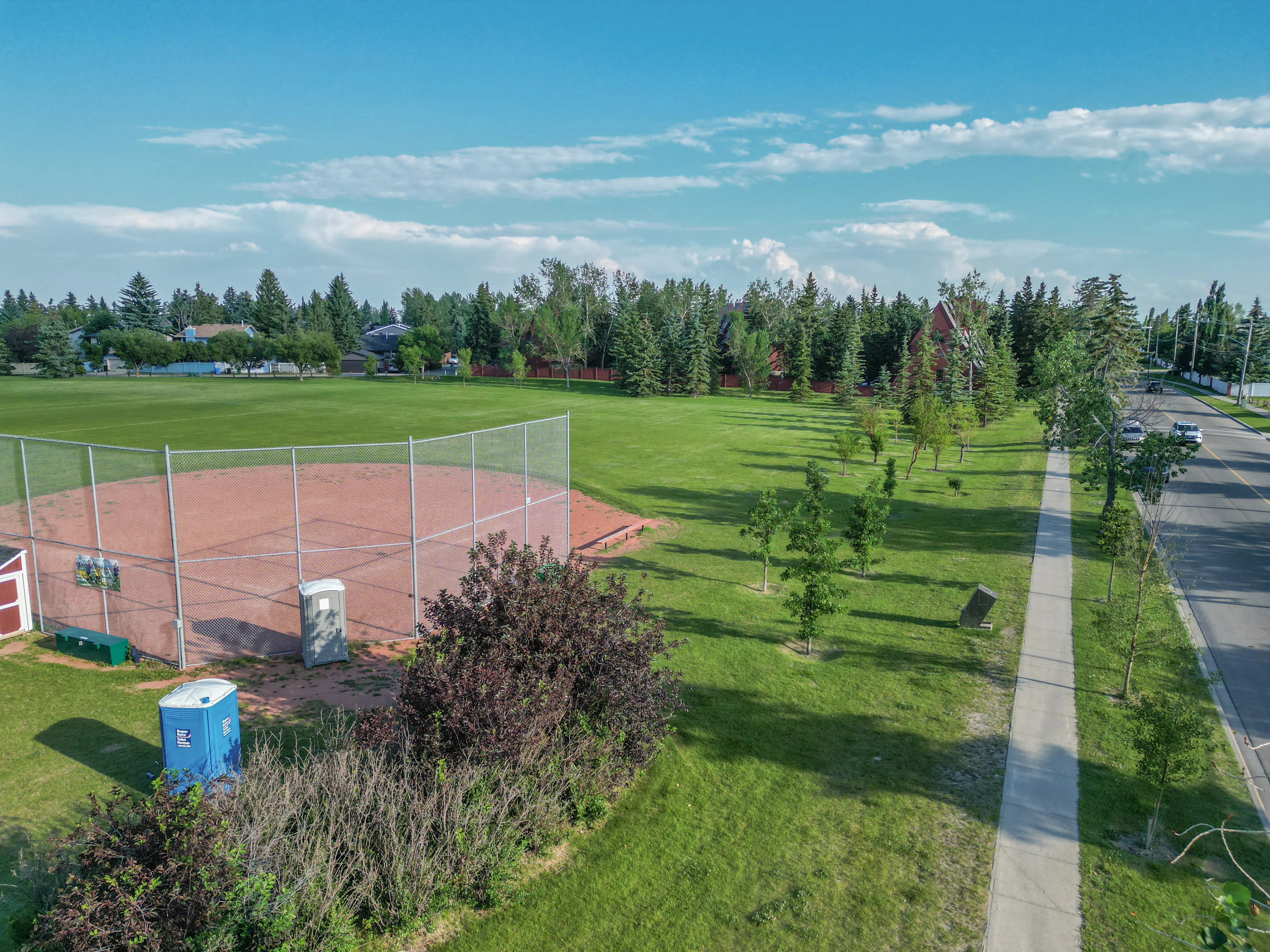 Grassy park with a ball diamond and a paved pathway lined with trees