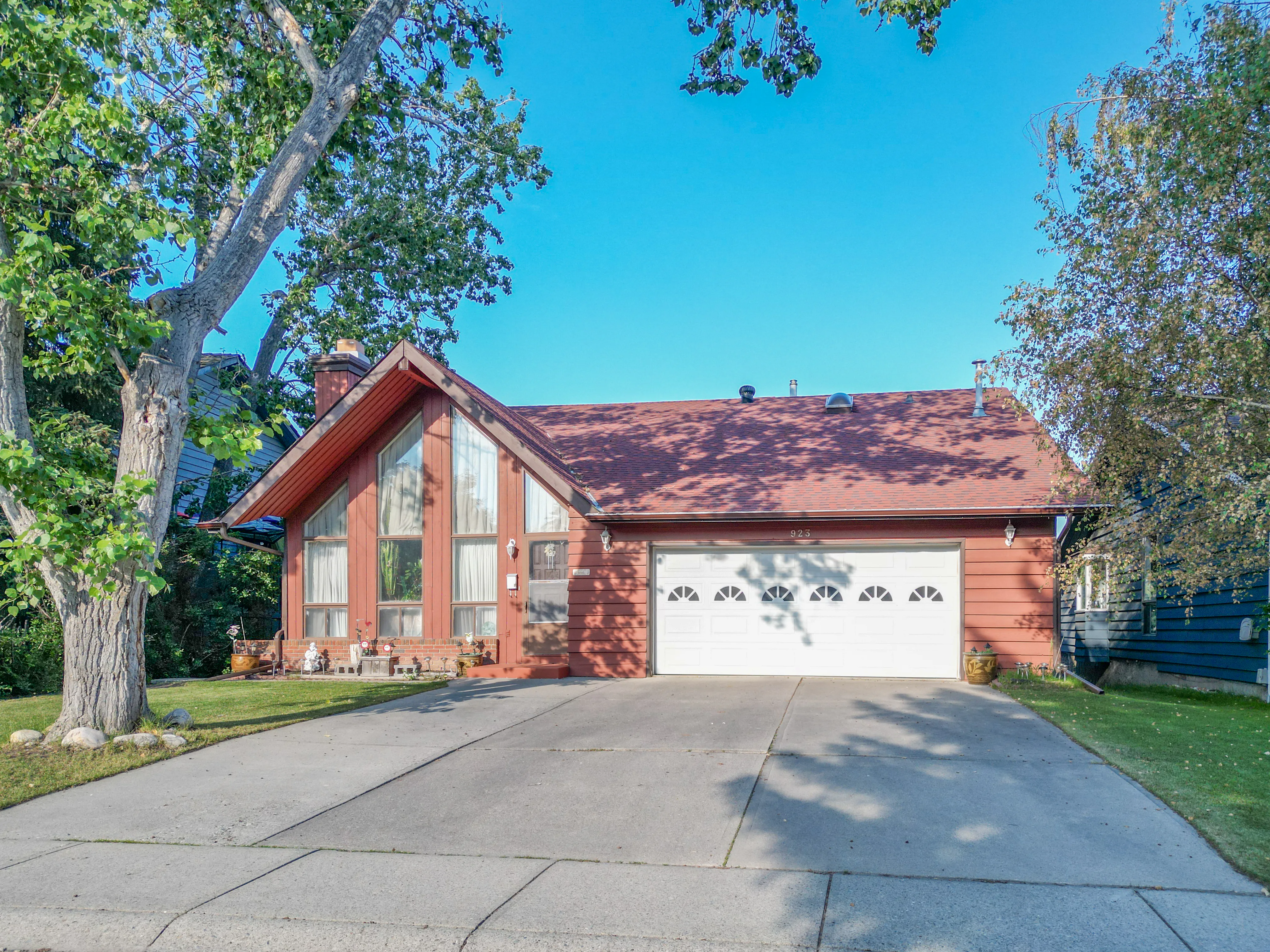 Two-storey home with a red roof and double garage among tall evergreens