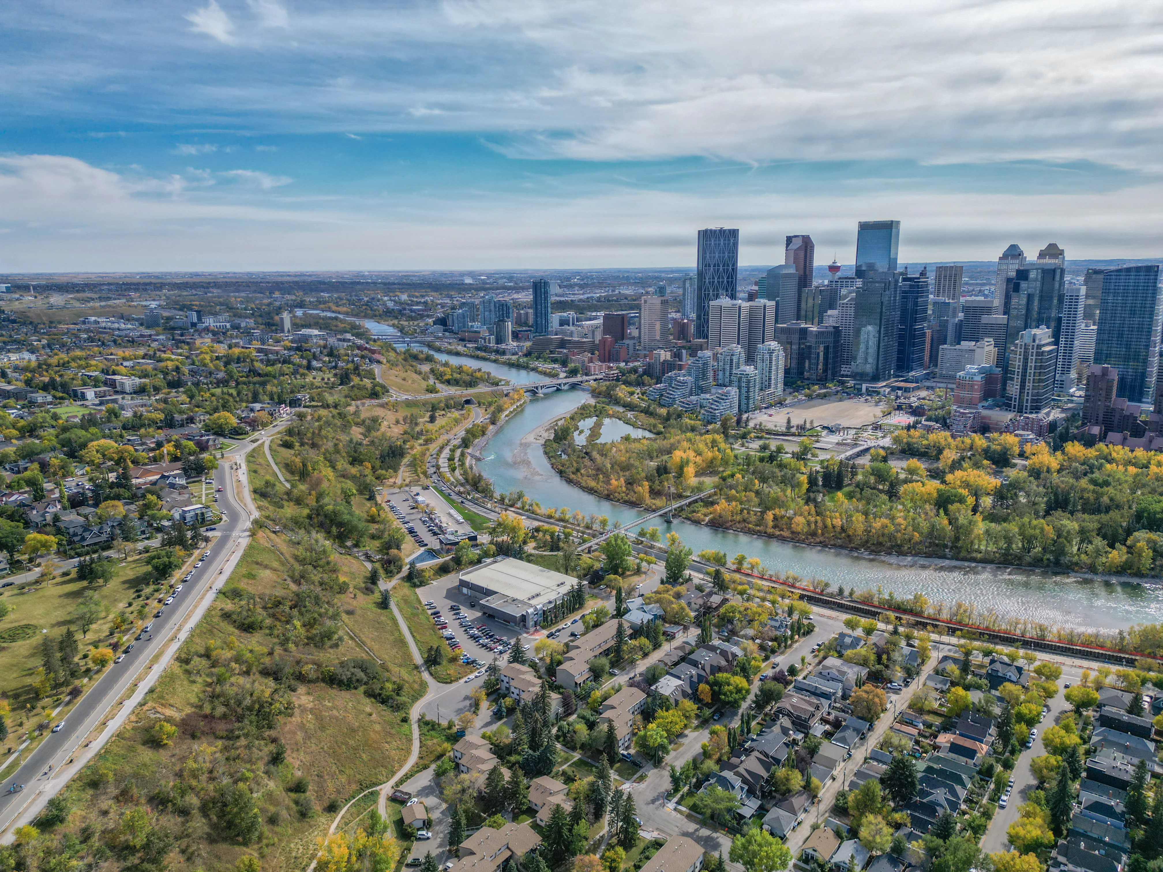 Aerial of a river valley with pathways and parkland below a city skyline