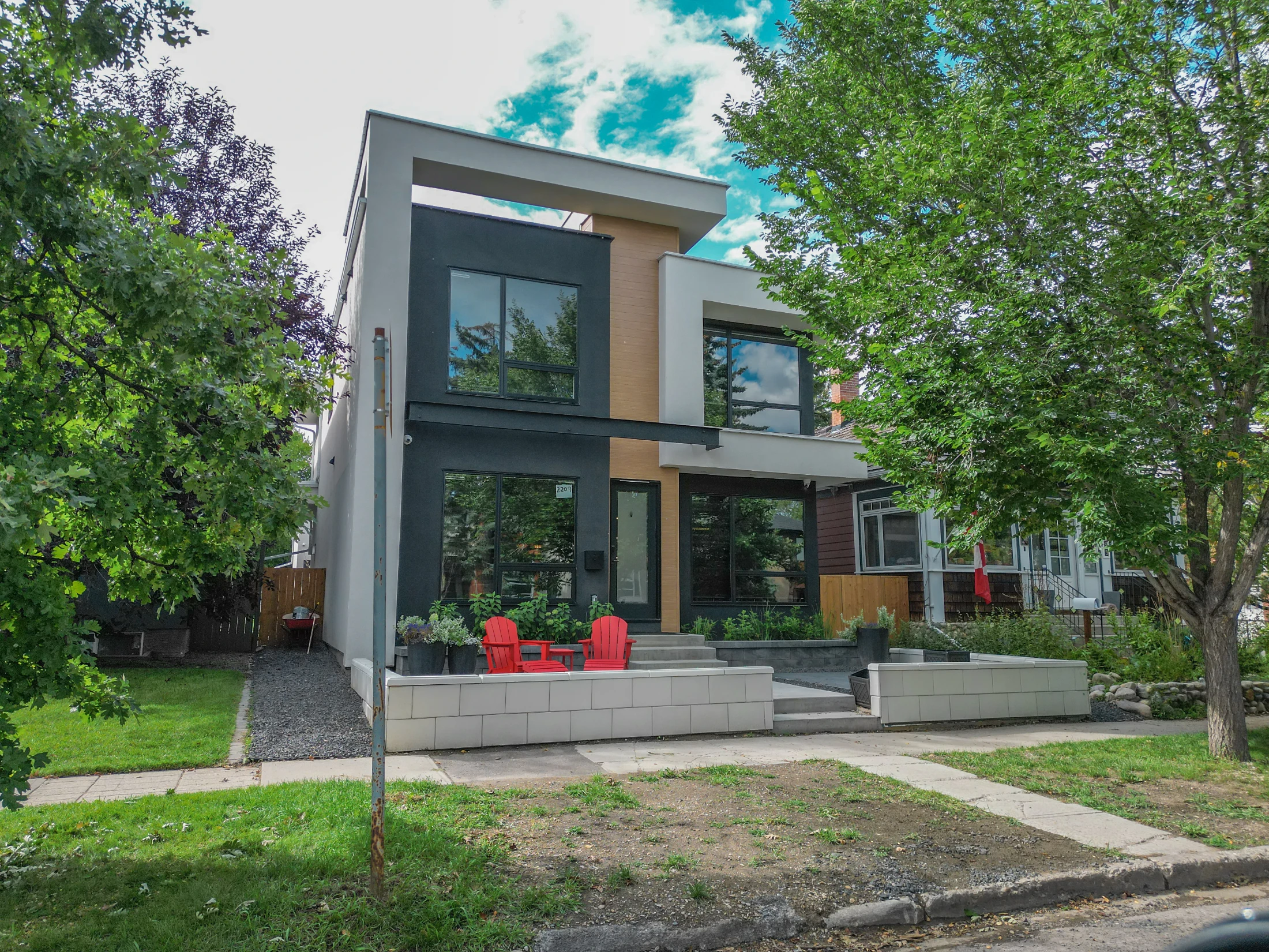 Modern infill home with dark siding and a front patio on a tree-lined street
