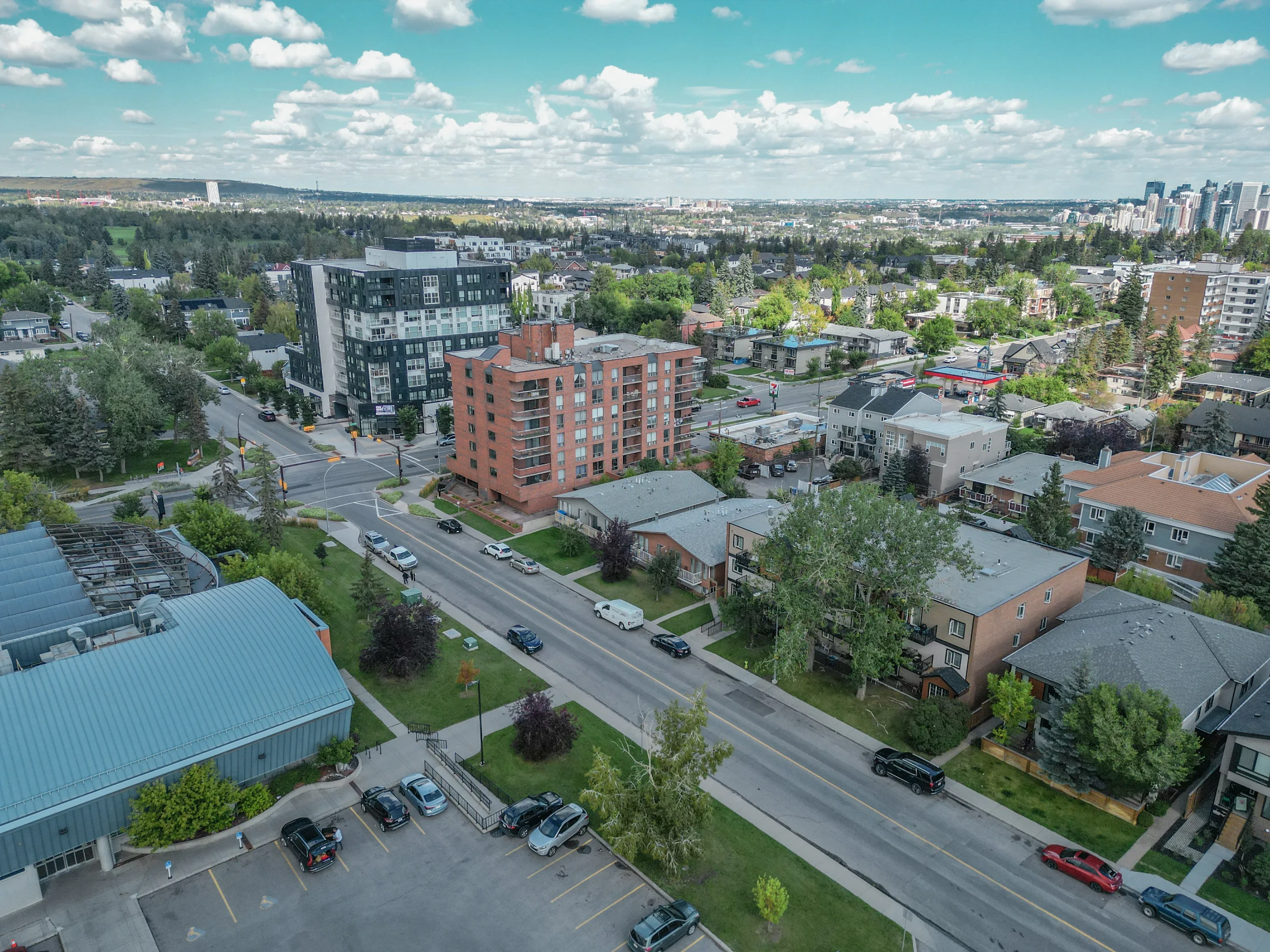 Aerial of a tree-lined inner-city street with low-rise condos and the downtown skyline