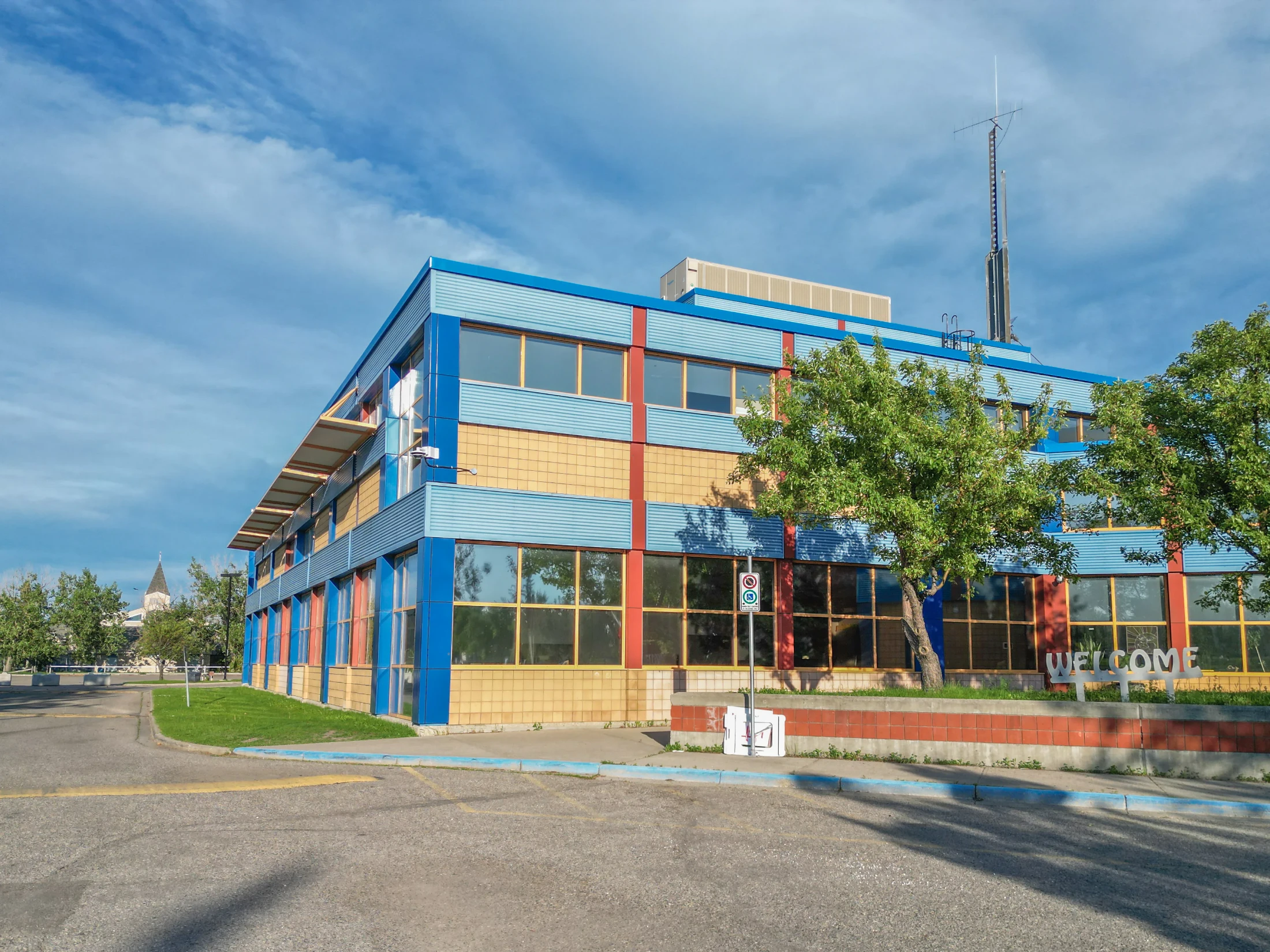 School building with blue and red panels and mature trees