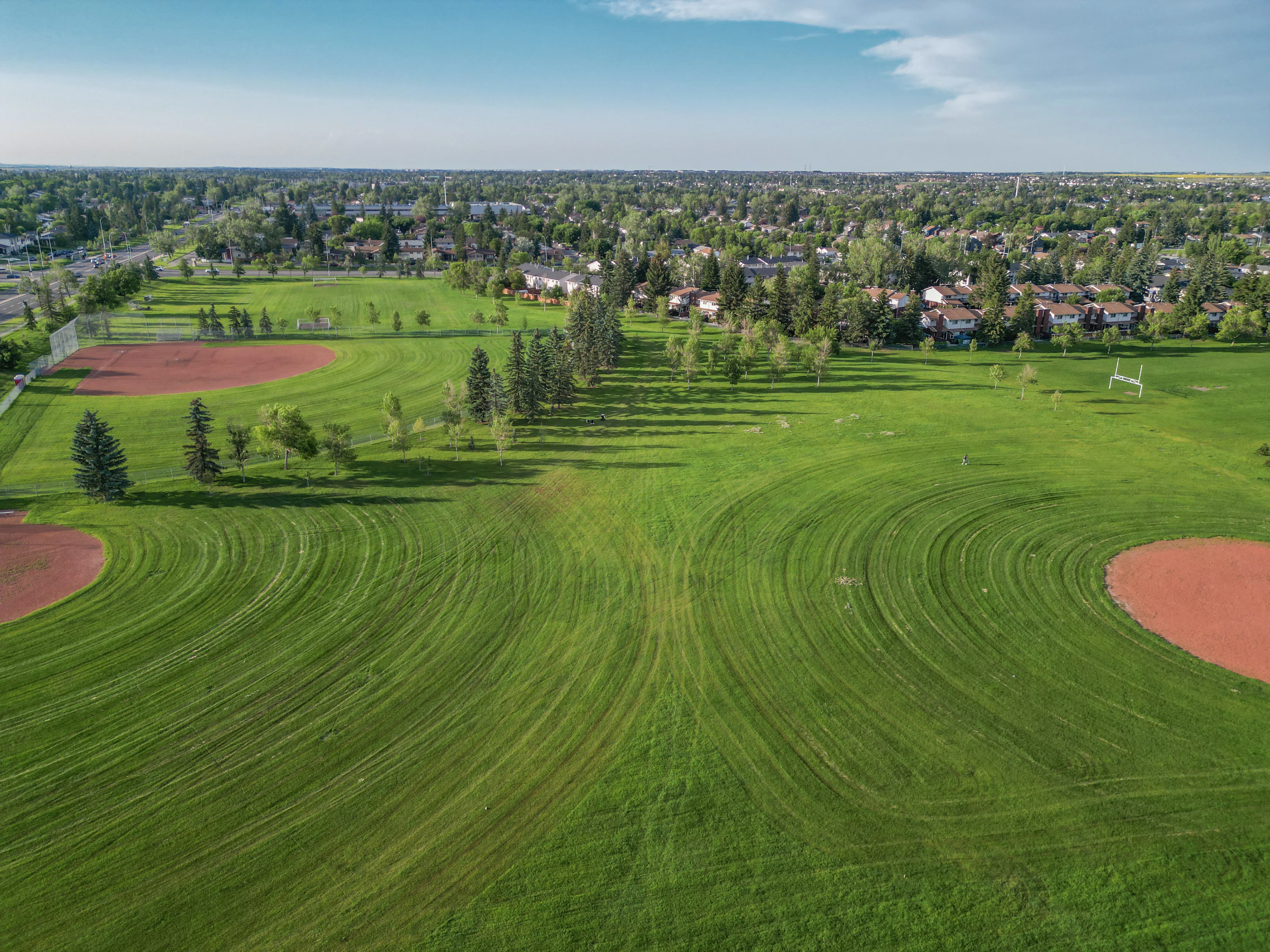 Large grassy sports field with a ball diamond beside a school