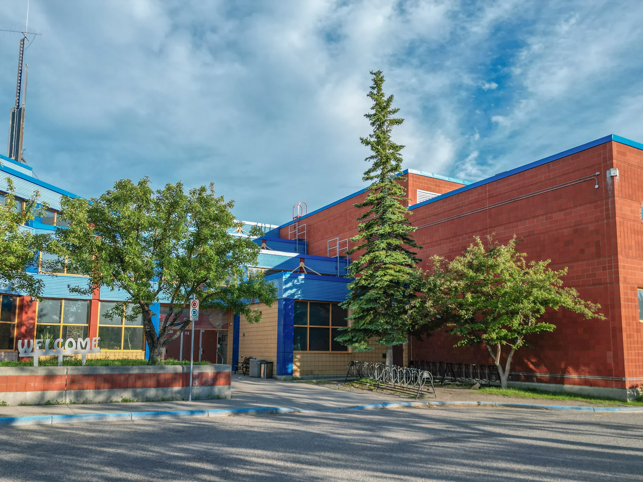 Brick school building with blue trim and mature spruce trees