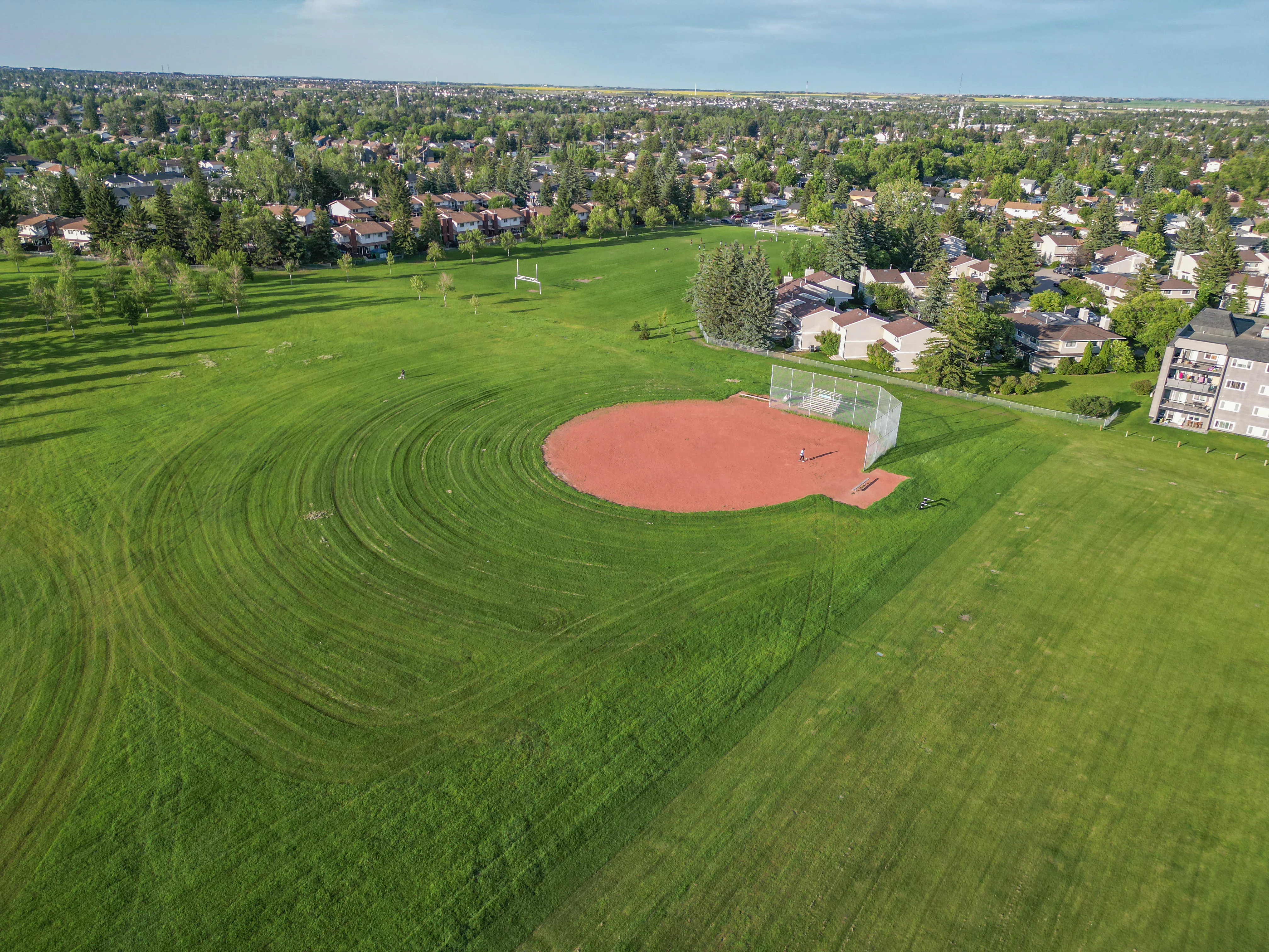 Open grassy playing fields with a ball diamond and trees