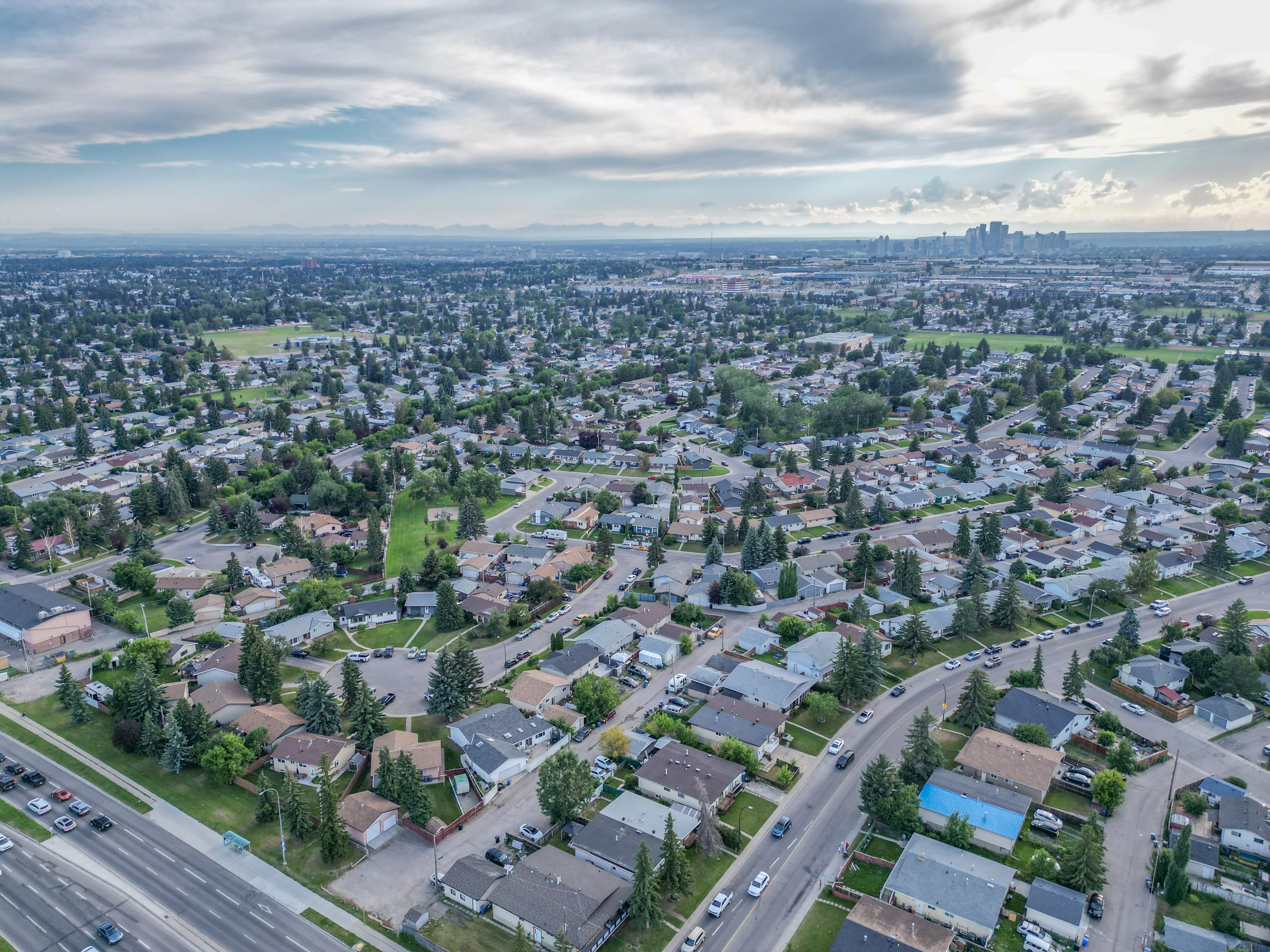 Wide aerial of homes and green space under a cloudy sky