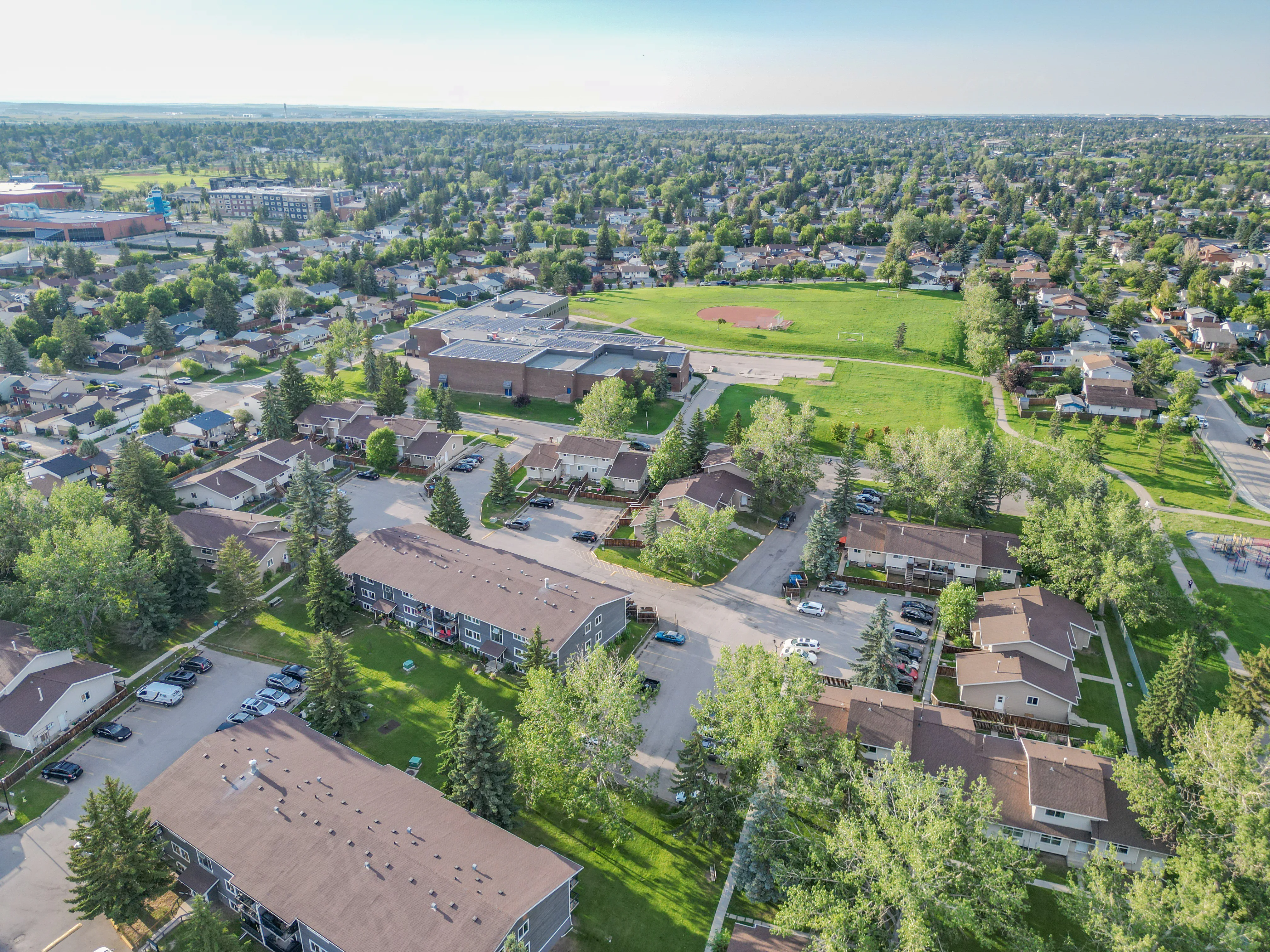 Aerial of townhomes and a green field with mature trees