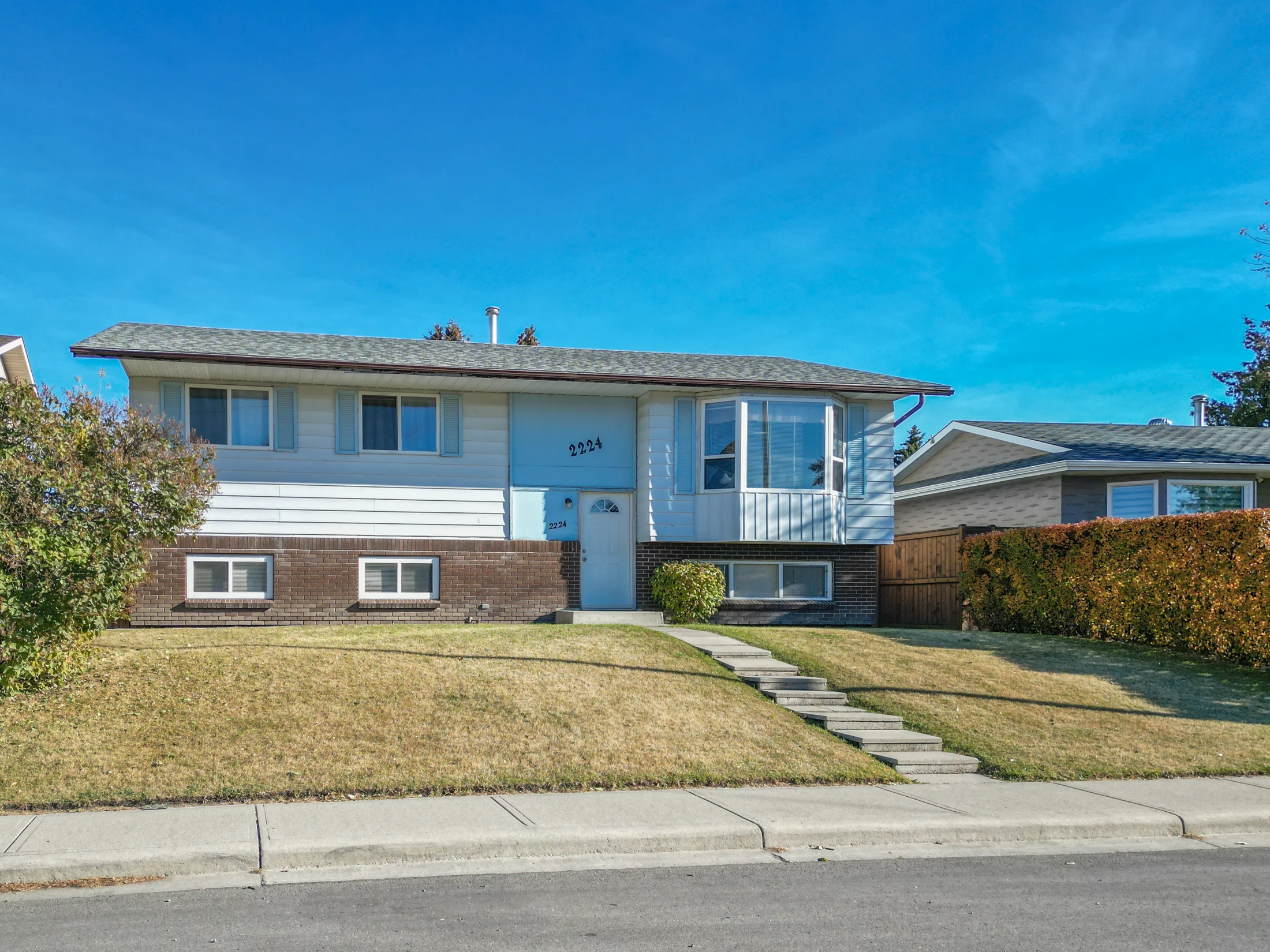 Bi-level home with a front lawn and a hedge
