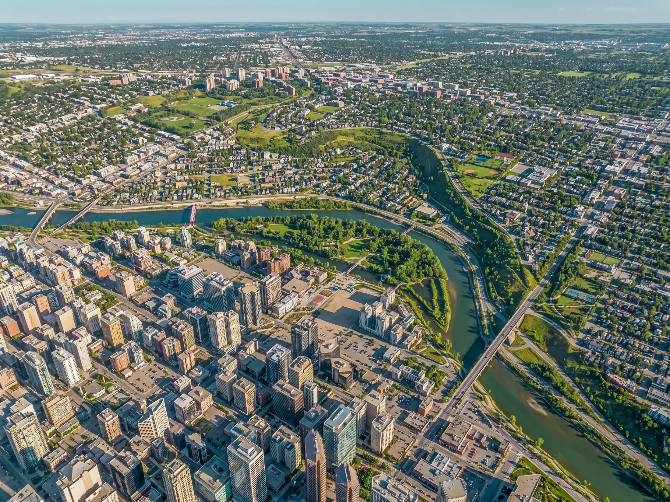 Aerial of the Bow River bending past downtown towers and parkland