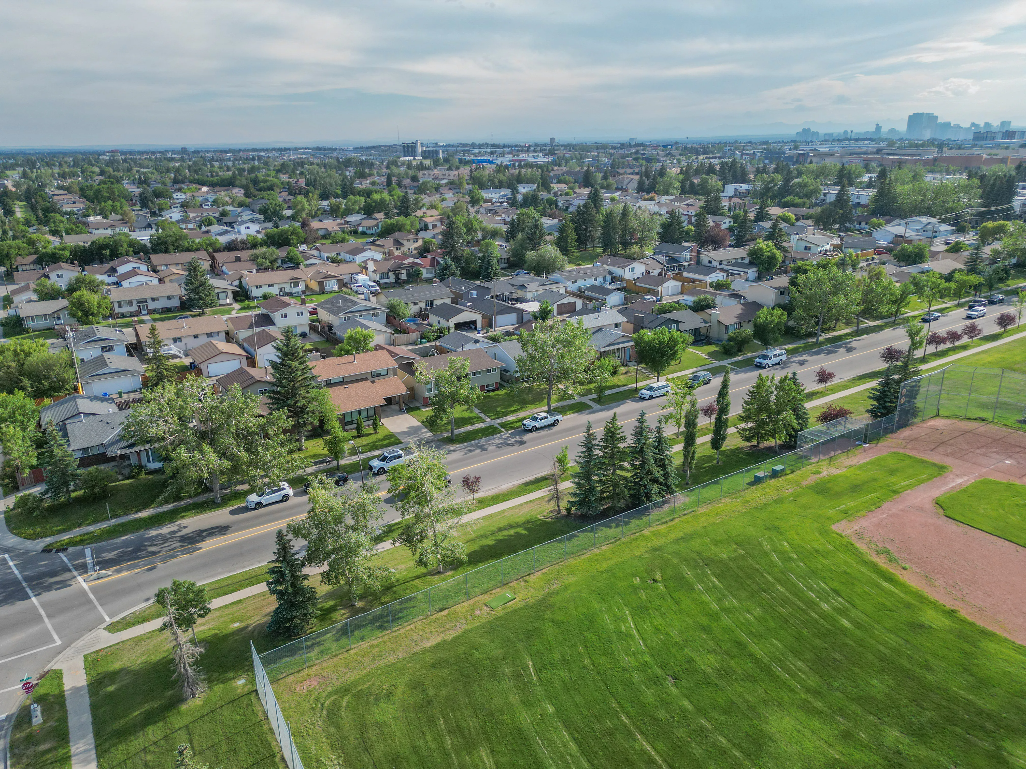 Aerial of a large green field beside a residential street