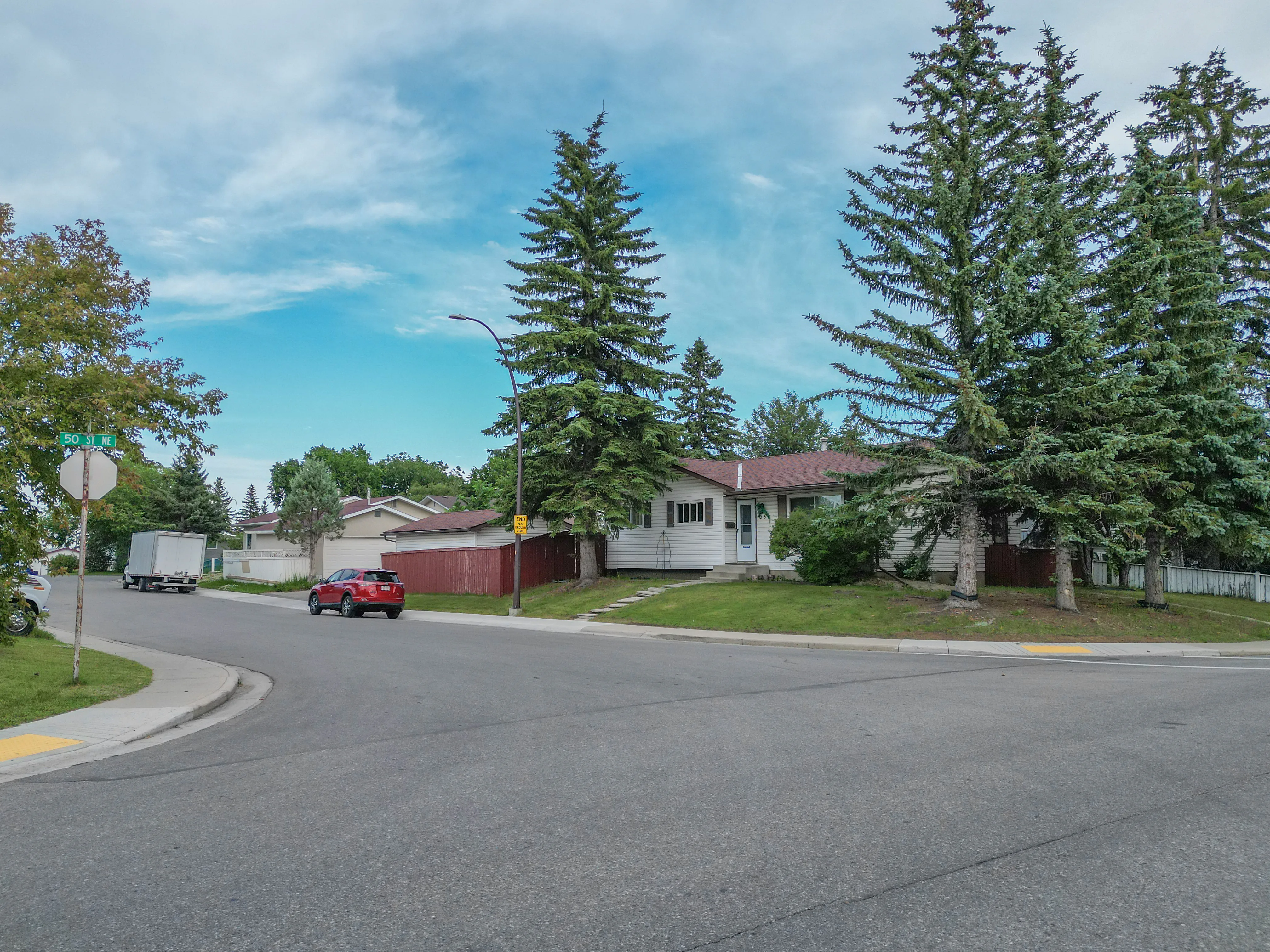 Bungalow with a corner lawn and tall evergreen trees