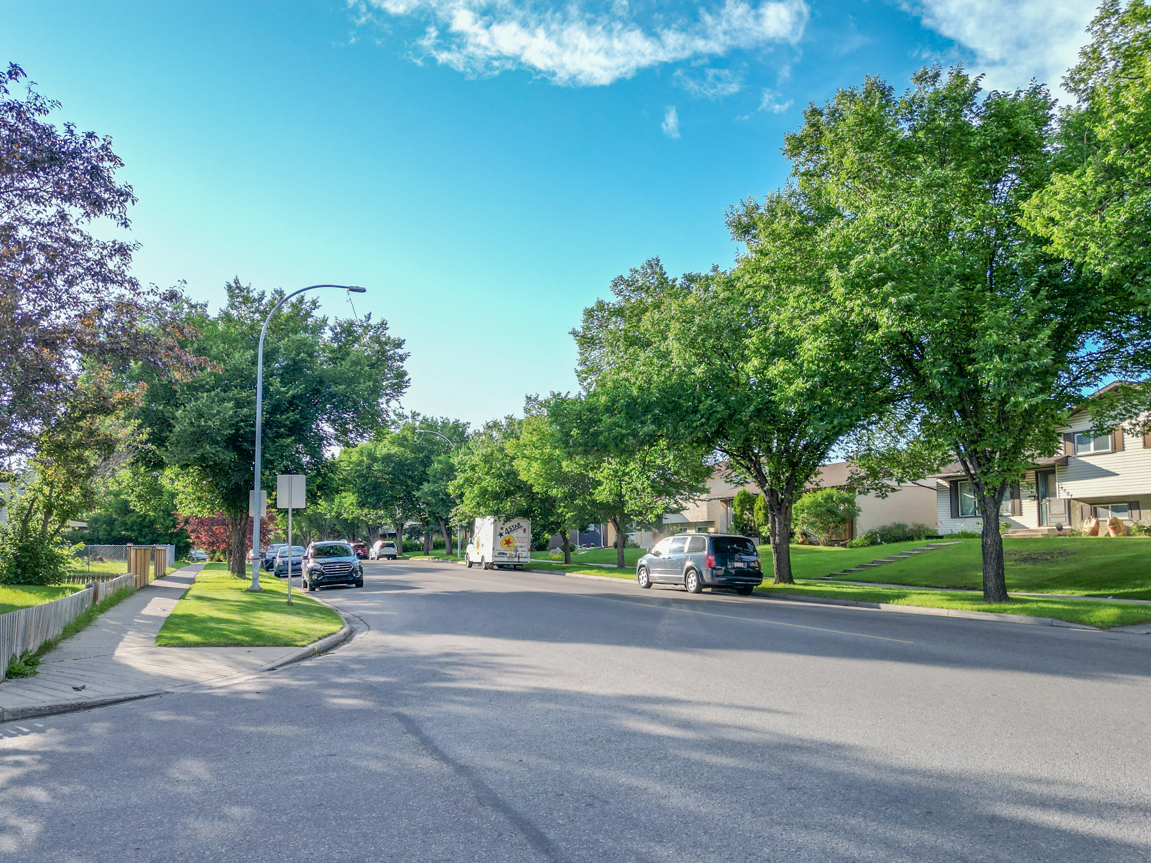 Tree-lined residential street with bungalows and parked cars