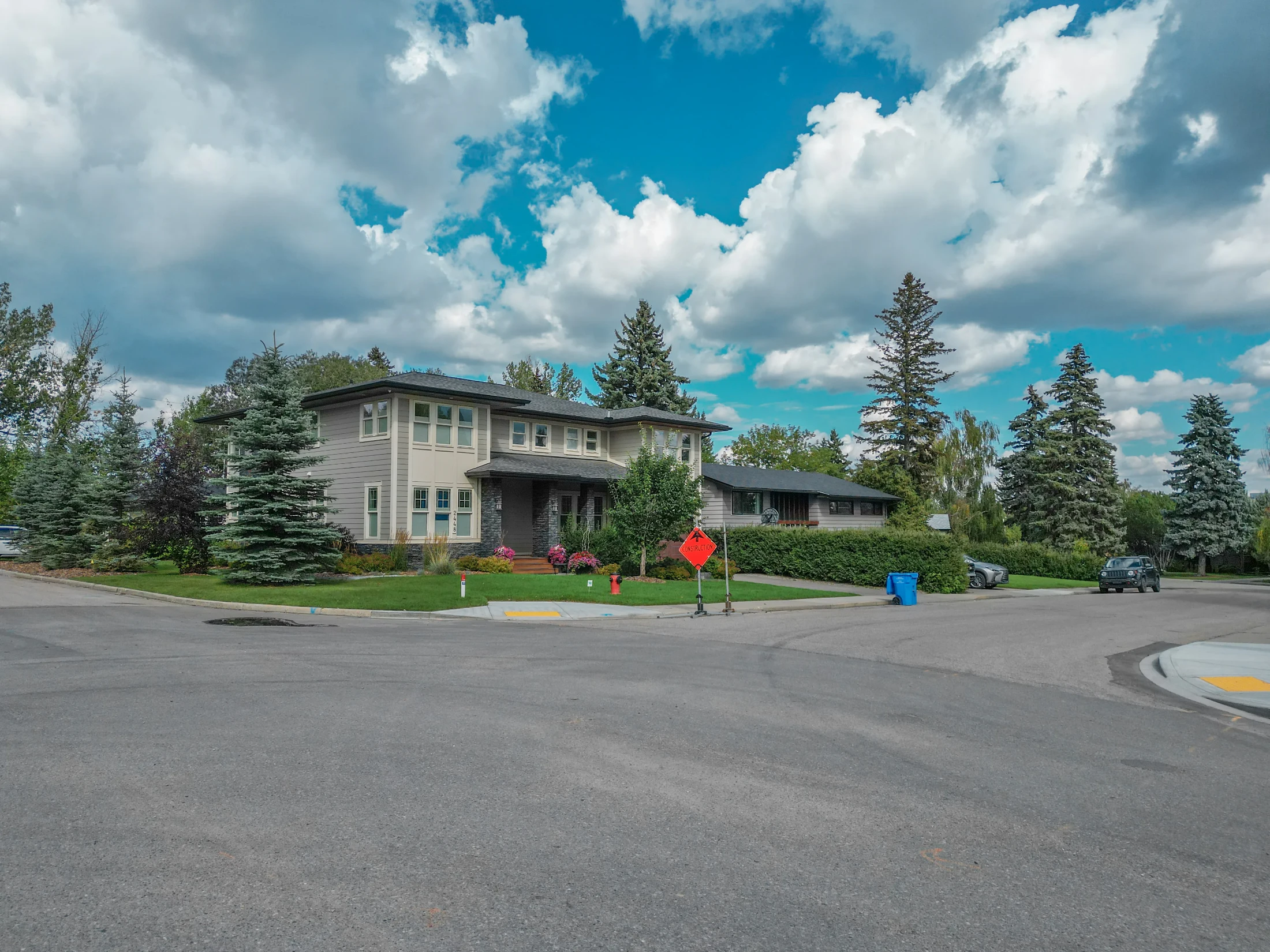 Two-storey home with a red maple and tall spruce trees on a corner lot